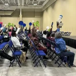 MUSC Senior Expo: a group of seniors doing chair yoga. 'Chair Yoga, get fit while you sit!'